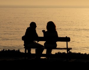 A couple sitting on a bench near a lake at sunset.