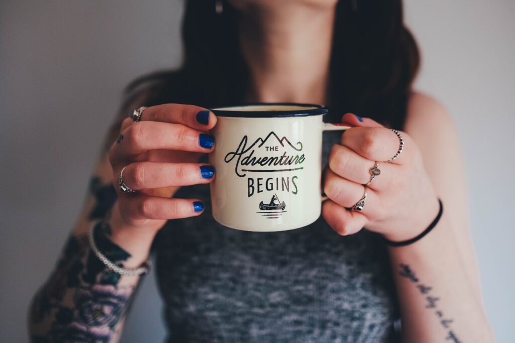 Lady holding a coffee mug that says "Let the Adventure Begin"